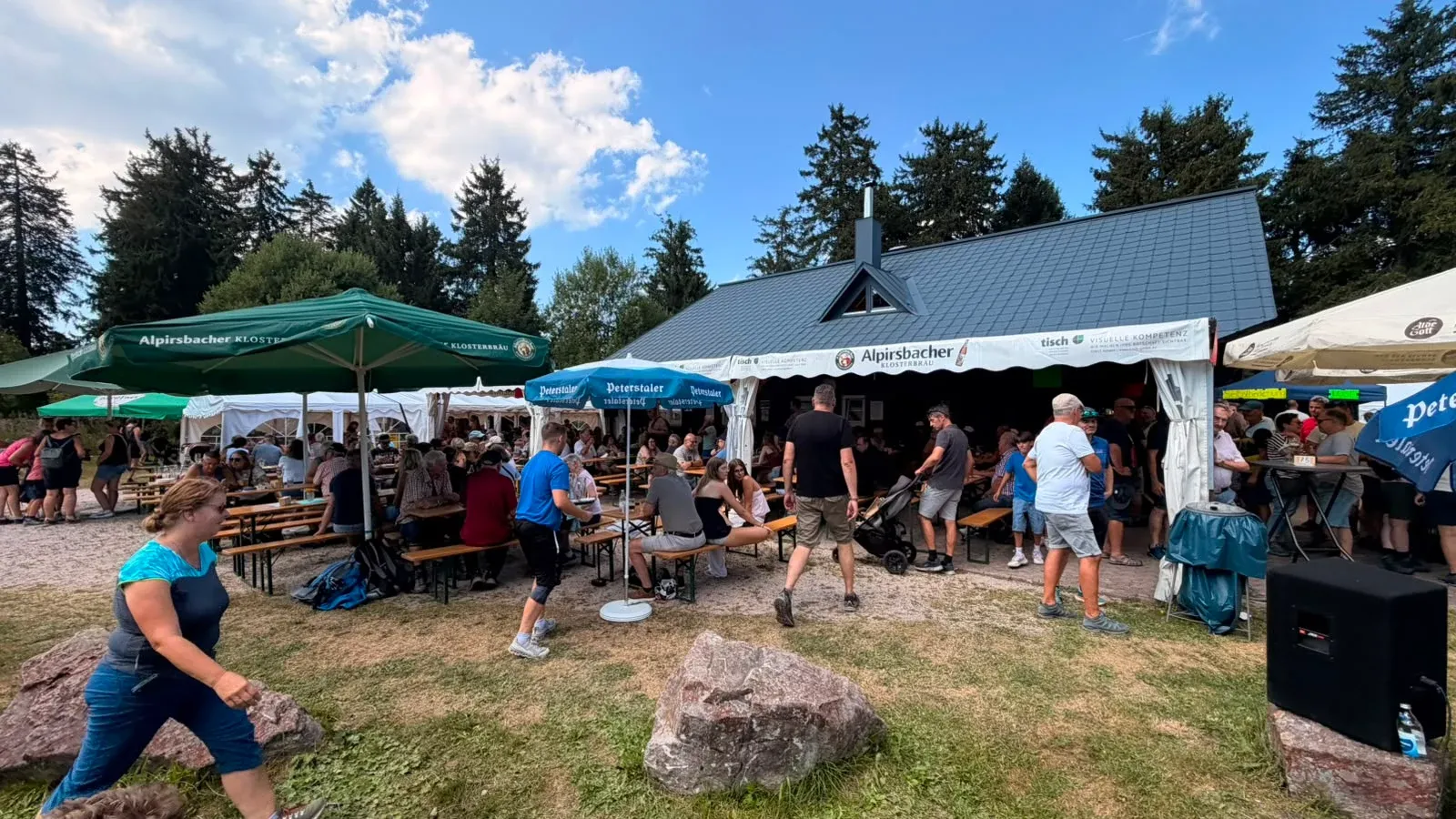 Gäste an Tischen und unter Sonnenschirmen vor der Skihütte.