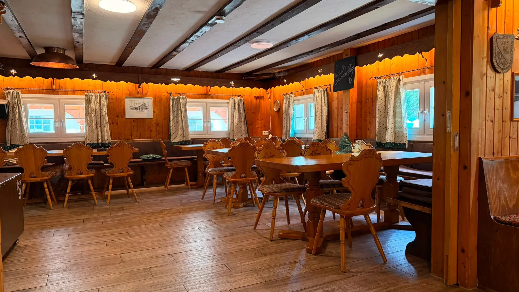 Holzverkleideter Gastraum der Skihütte mit langen Tischen und Stühlen.