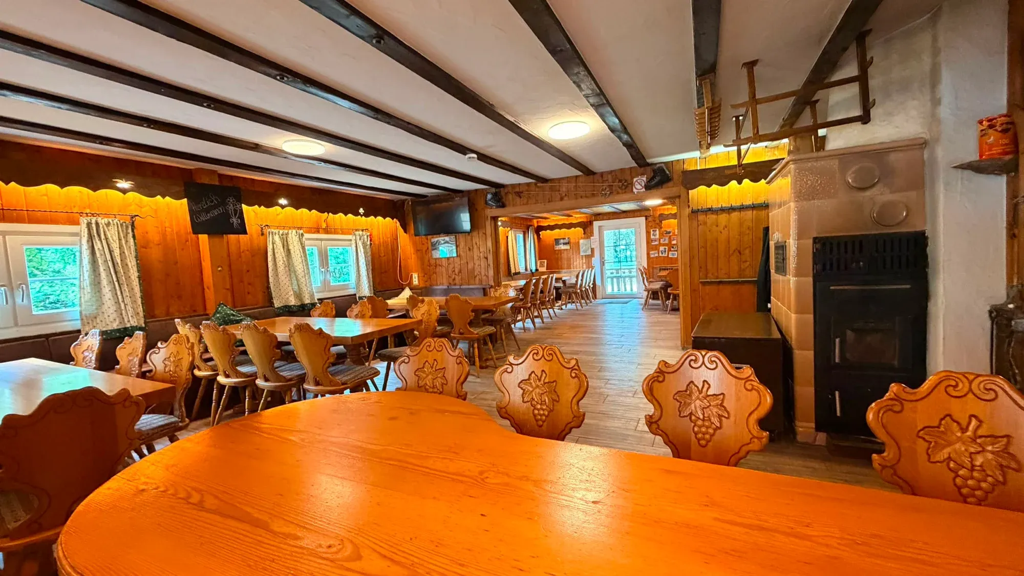 Holztische, Stühle und Deckenbalken im Aufenthaltsraum der Skihütte.