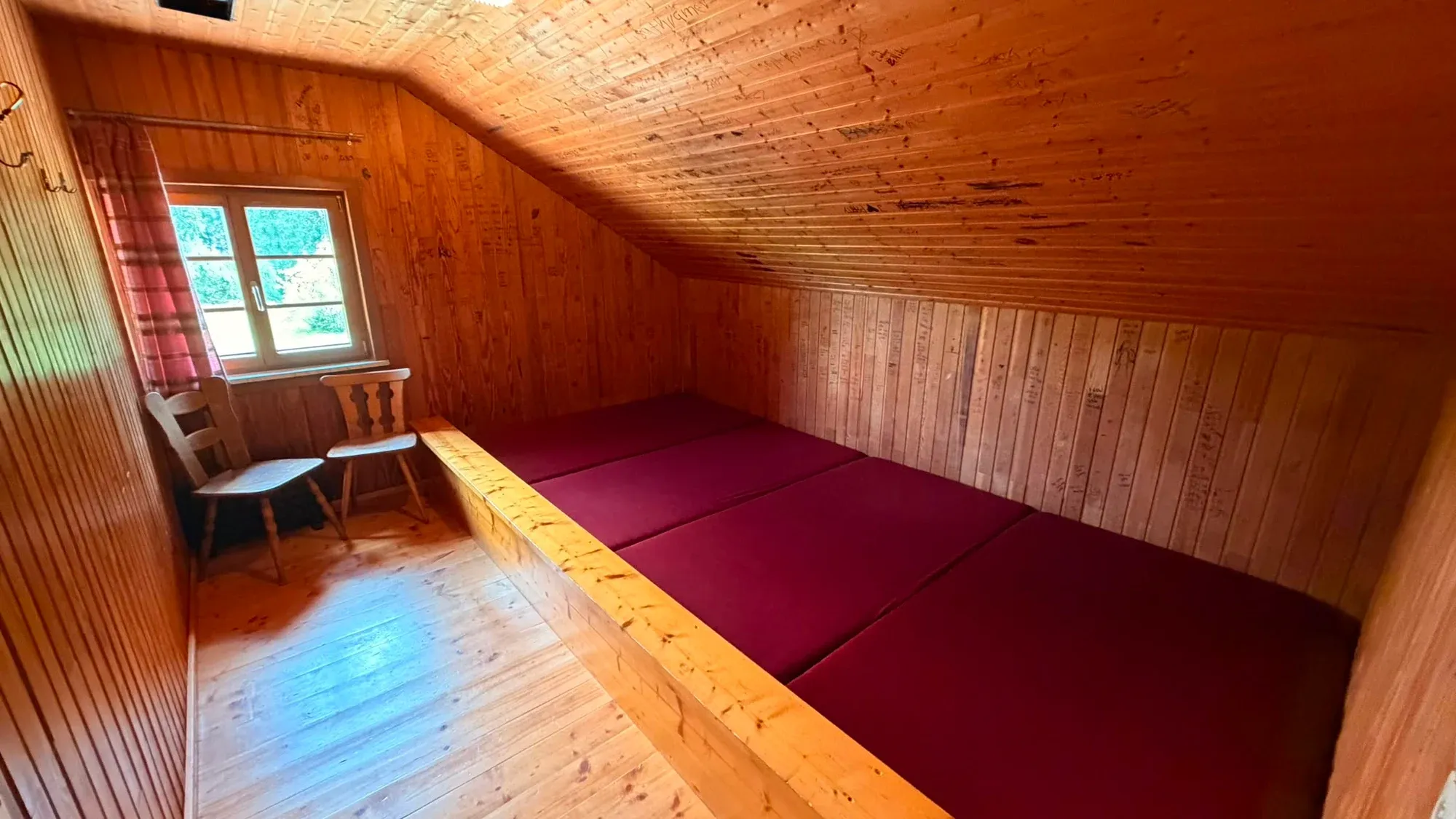 Holzverkleideter Schlafraum mit einem niedrigen Doppelbett und Dachschräge.