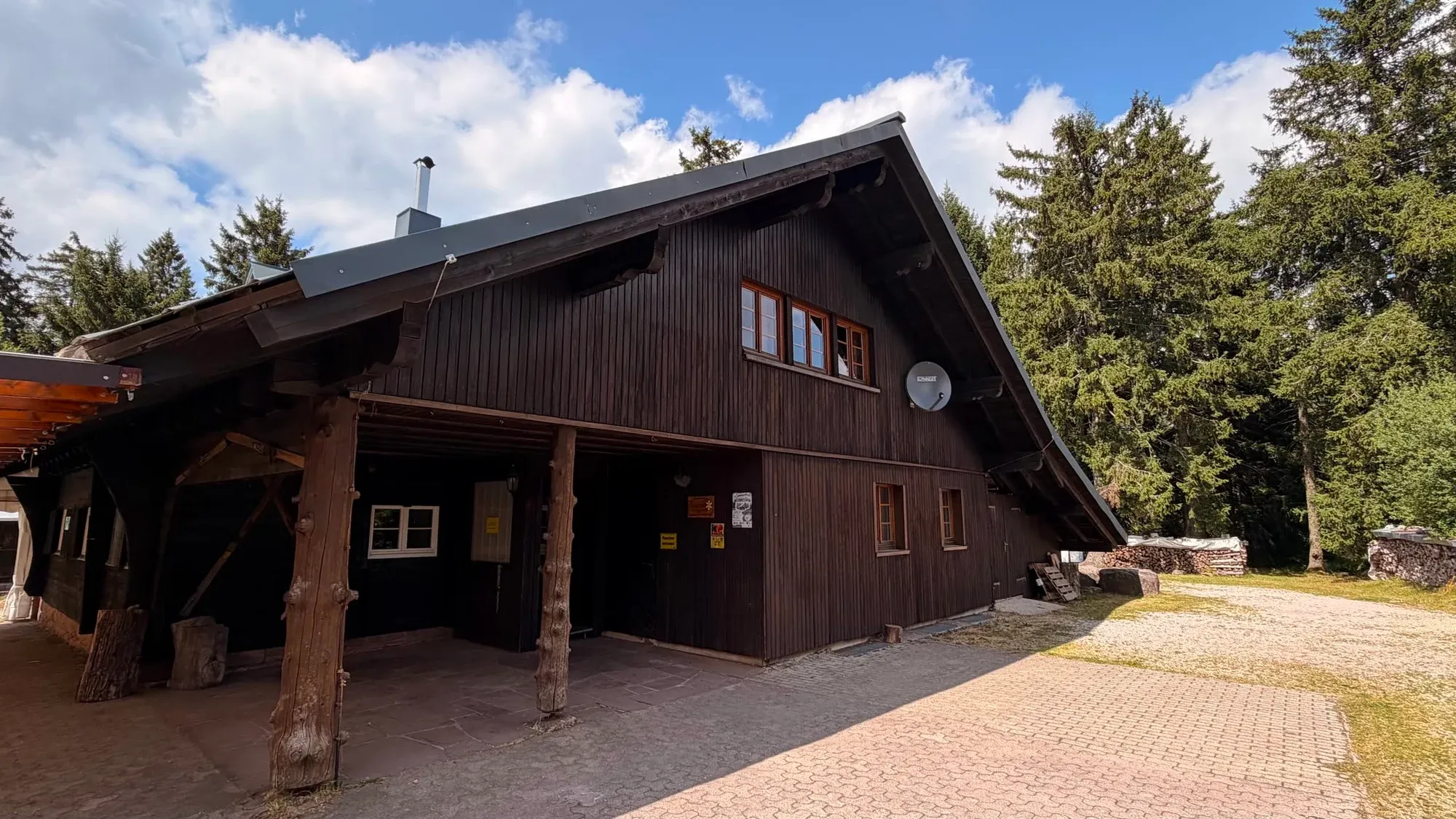 Außenansicht unserer Skihütte mit Holzbänken und überdachtem Eingang im Sommer