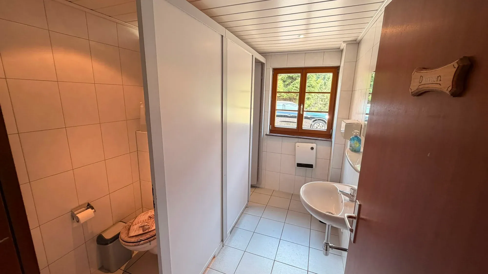 Heller gefliester Sanitärbereich mit Fenster und Toilette.